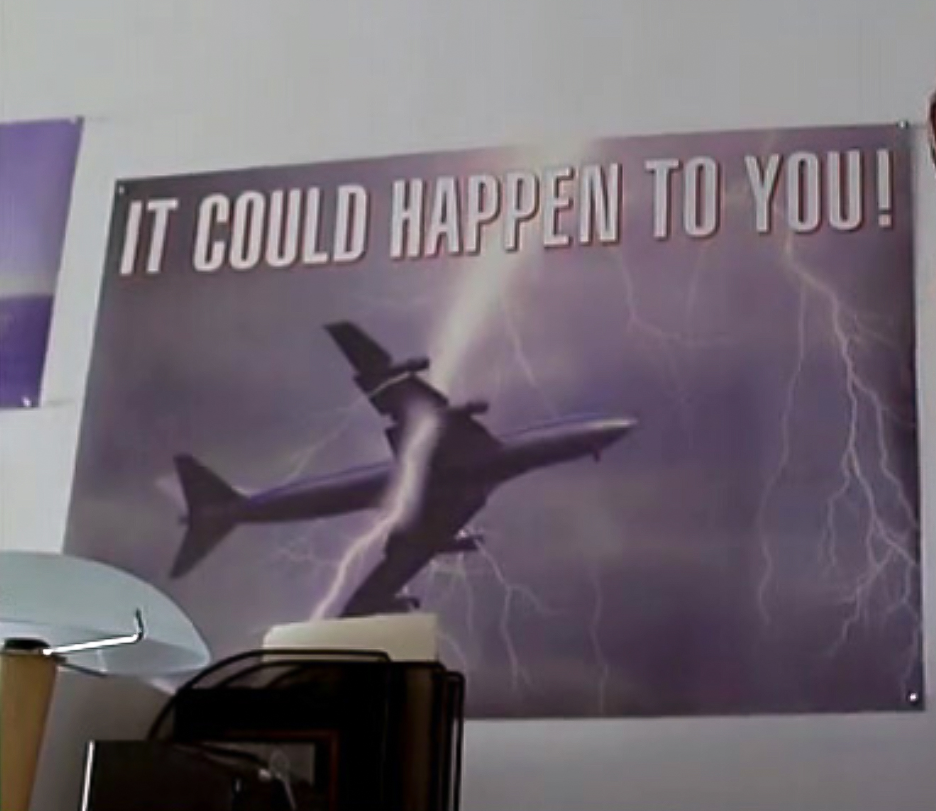 Bild eines aufgehängten Posters an einer Wand. Zu sehen ist ein Flugzeug, welches vom Blitz getroffen wird. In Versalien der Schriftzug "It could happen to you!"